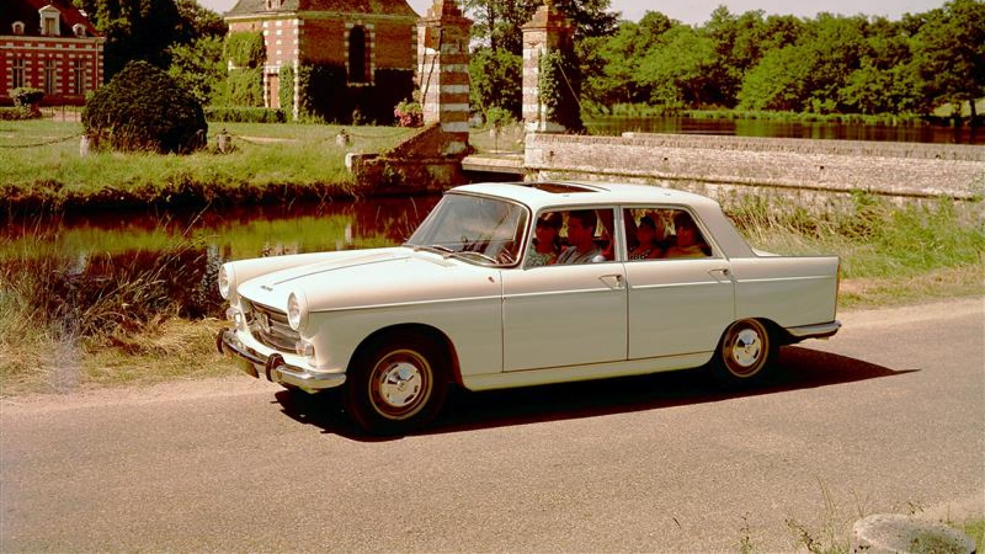 PEUGEOT 404 auf einer Landstraße vor einem Schloss aus rotem Backstein, umgeben von Grün