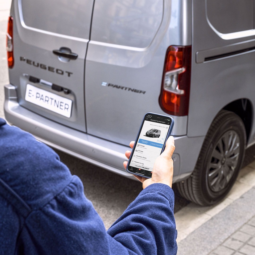 Frau benutzt hinter dem PEUGEOT E-Partner ein Smartphone